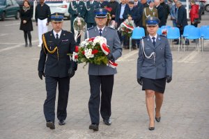 Delegacja Policji i Państwowej Straży Pożarnej podchodzi z wieńcem do pomnika.