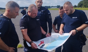 Policjanci trzymają w ręku mapę sztabową.