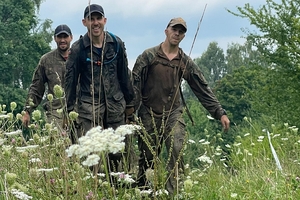 Mężczyźni w mundurach idą polną drogą przez łąkę.