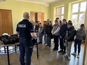 policjant pokazujący uczniom szkoły  podstawowej ubiór przeciwuderzeniowy