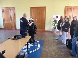 policjant pokazujący uczniom szkoły  podstawowej ubiór przeciwuderzeniowy