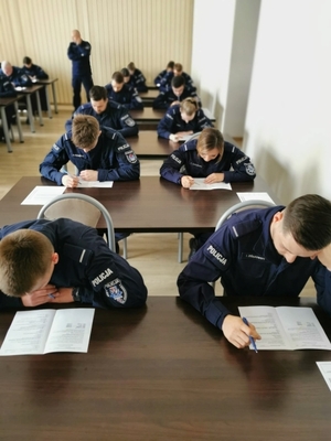 policjanci siedzący w ławkach i rozwiązujący test